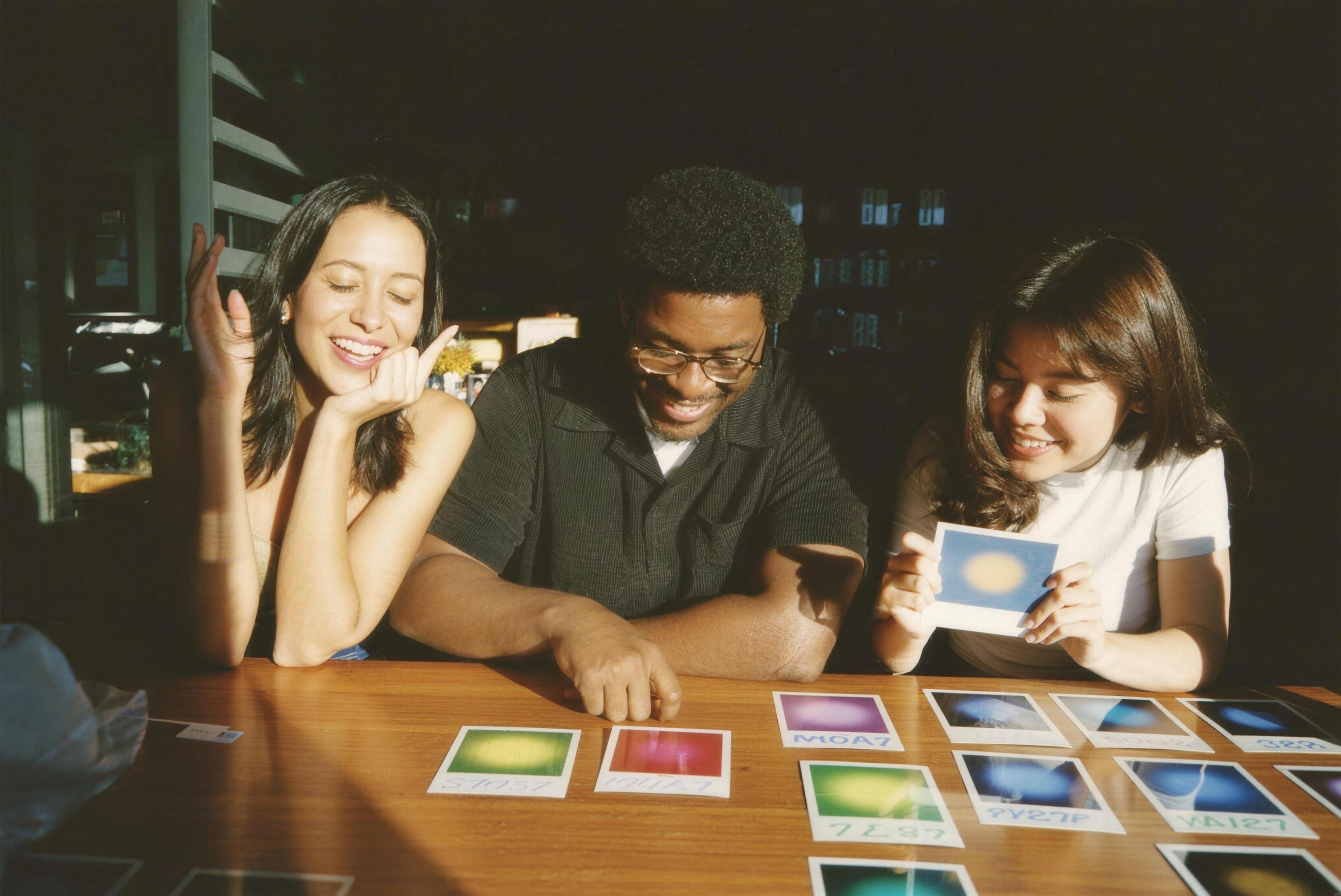 Three friends laughing over colorful aura photographs on a wooden table