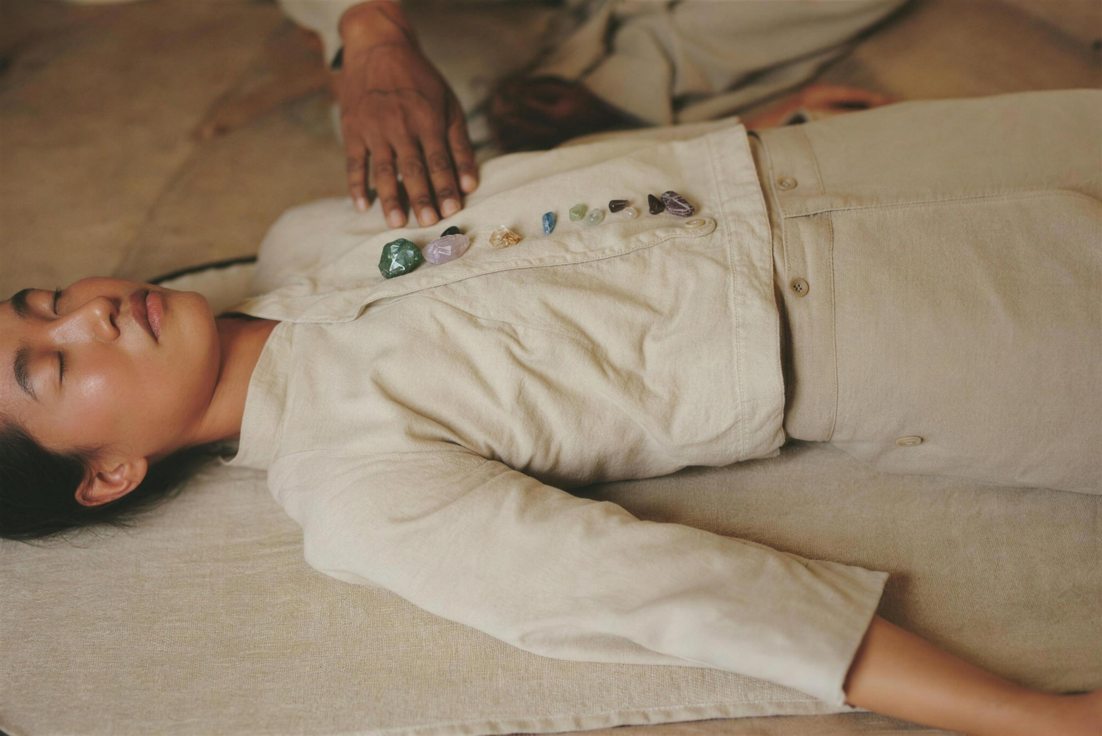 A woman resting on a linen mat with small crystals placed along her clothed torso