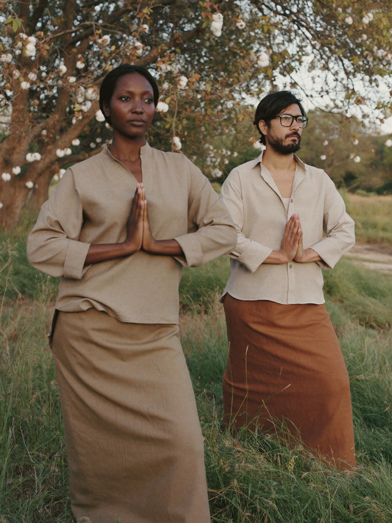 A Black woman and a Chinese American man practicing qi gong in a meadow under cottonwood trees at dawn. Modest clothing: loose long-sleeved linen