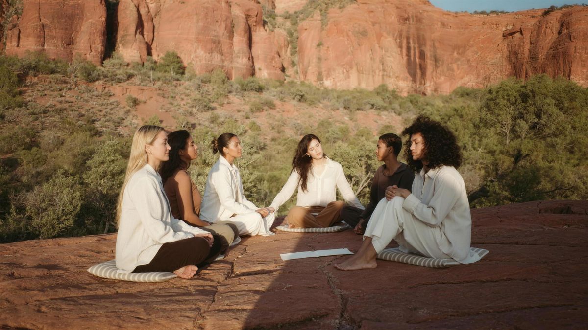 Retreat participants in long-sleeved linen sitting in a circle on red rock beneath the Sedona buttes at golden hour