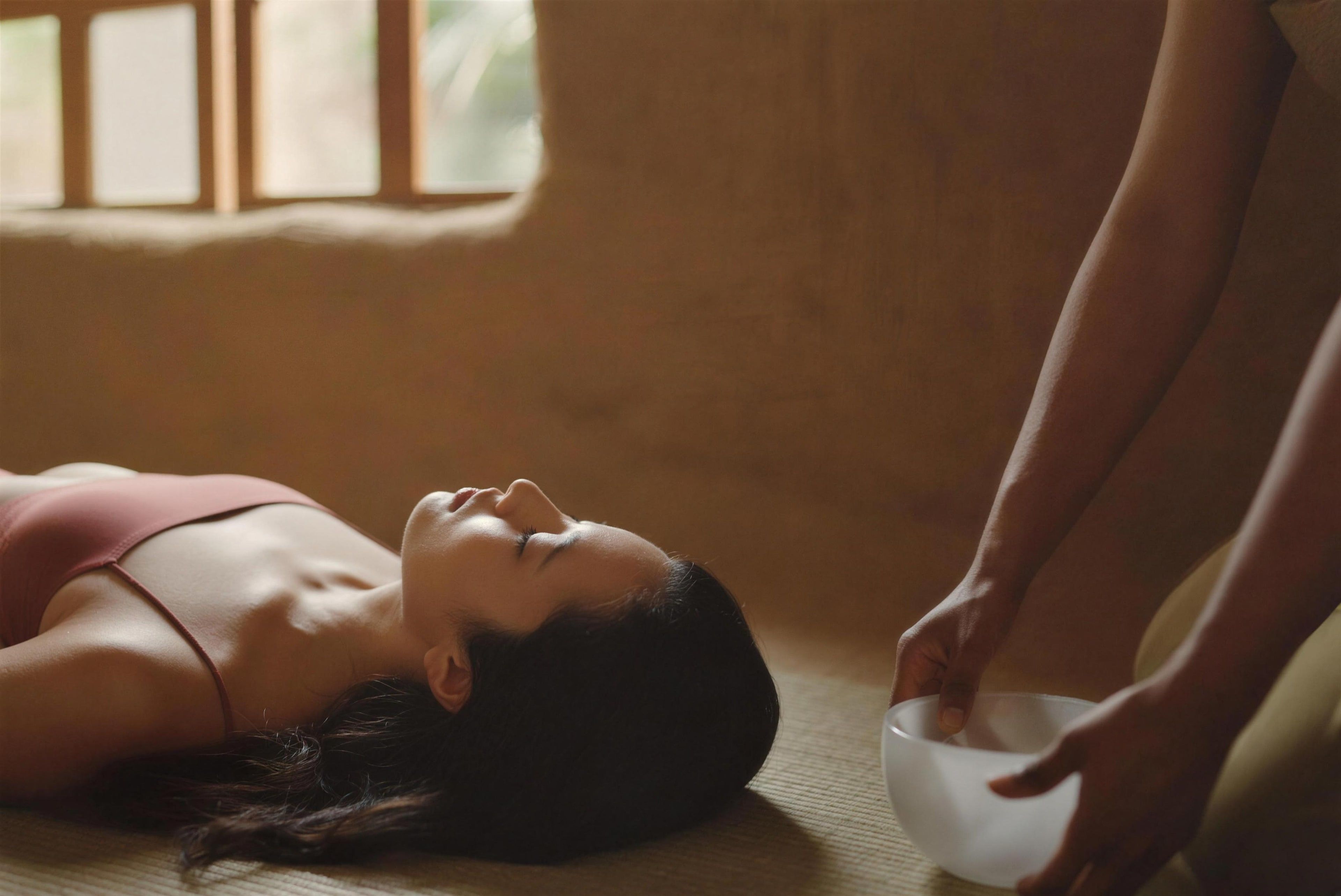 A woman resting during a sound bath as a crystal bowl is played beside her
