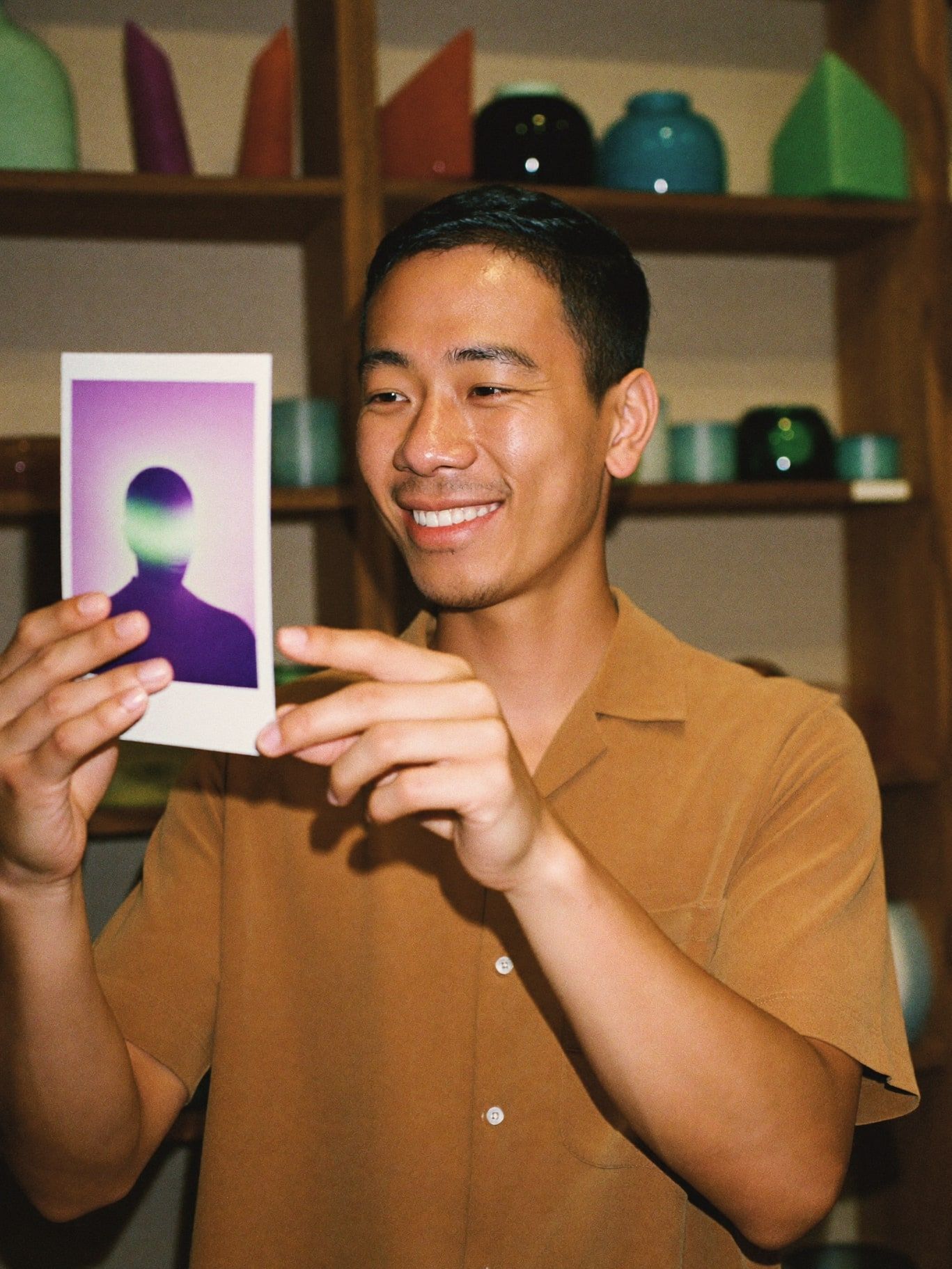 A Filipino man in his 30s with short black hair, wearing a sand linen shirt, smiling as he looks at his instant aura photograph glowing violet and