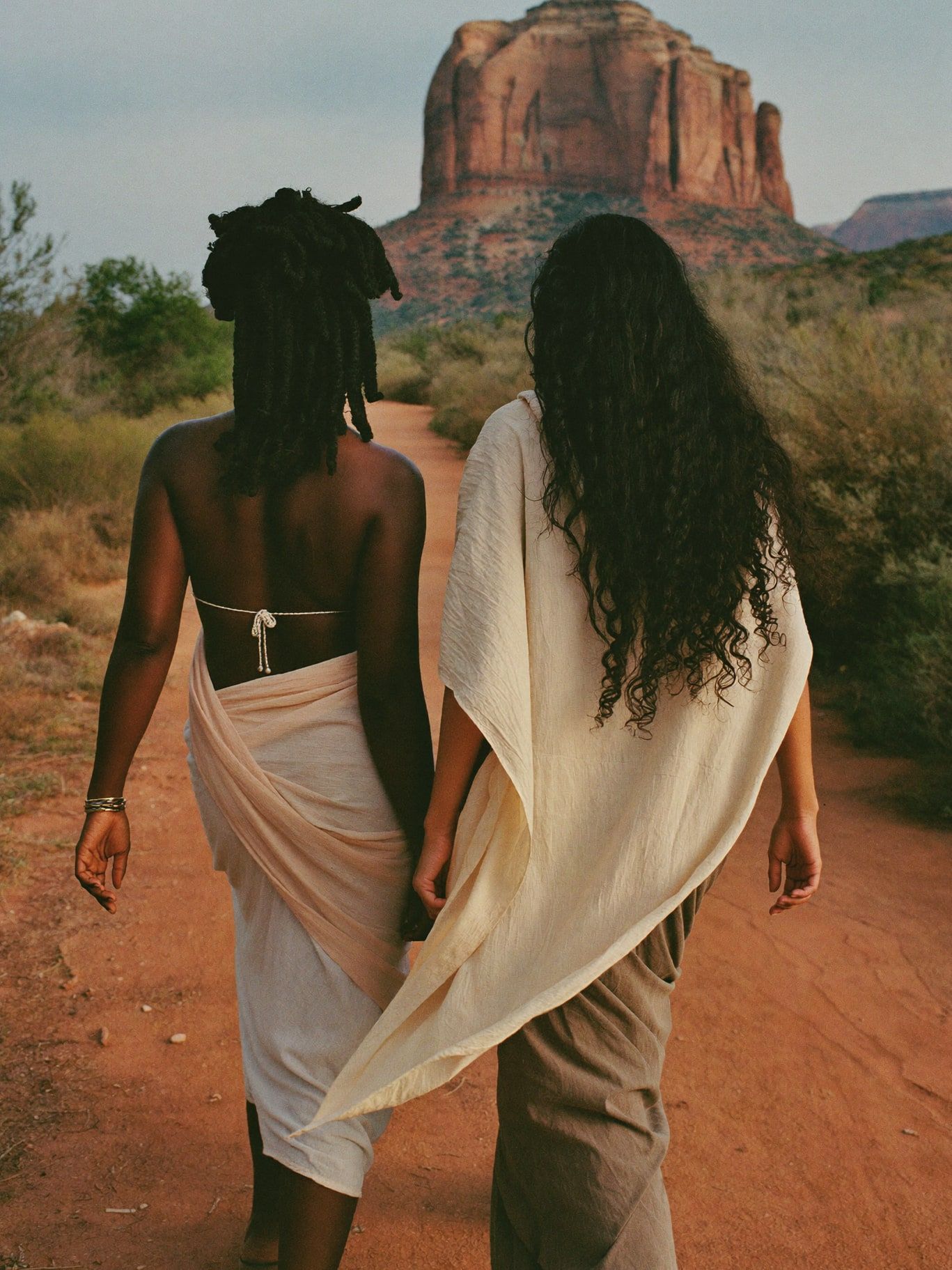 Two women walking a red dirt trail toward the buttes