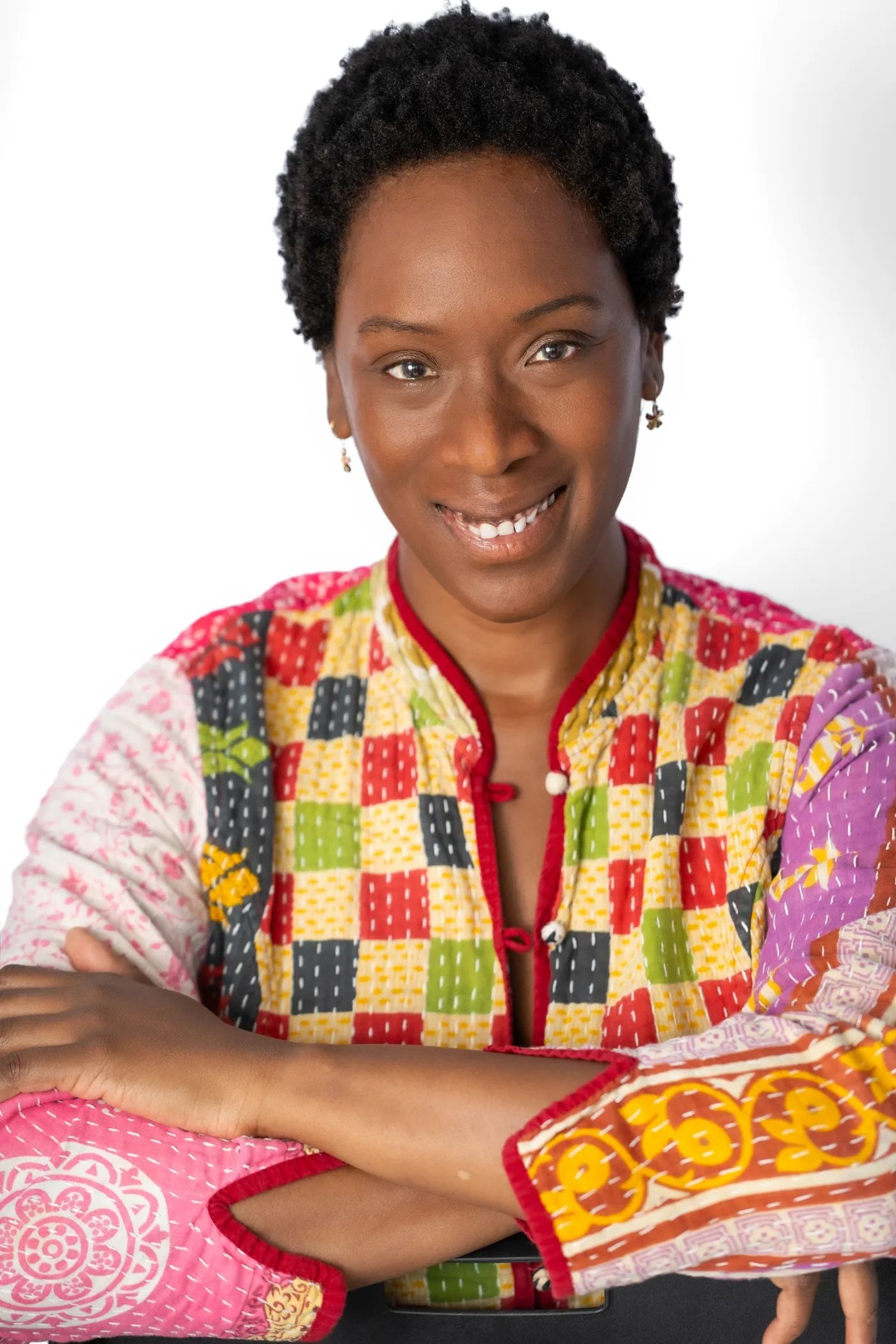 Yolessa smiling with her arms crossed, wearing a colorful patchwork jacket